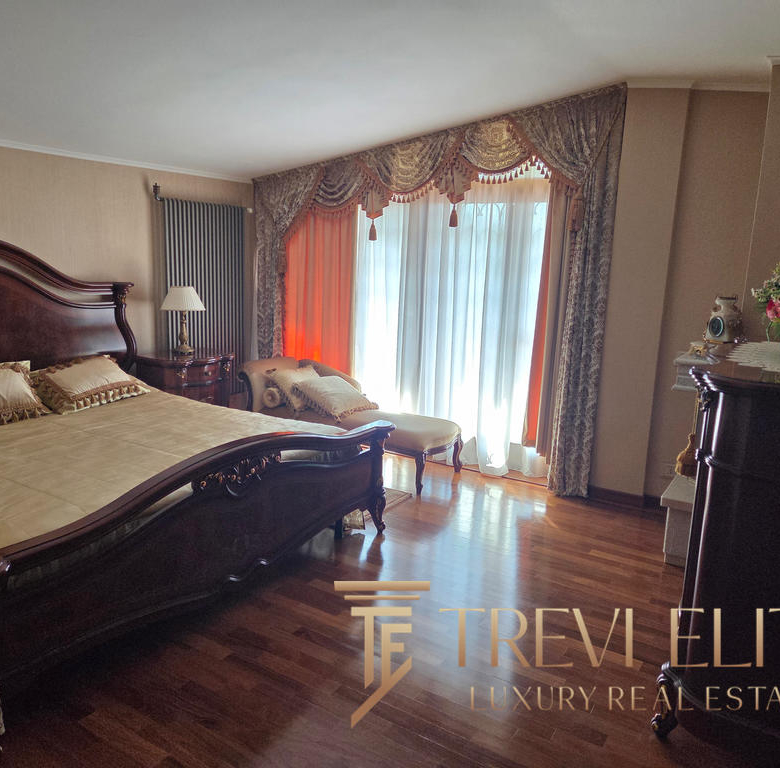 Elegant antique bedroom featuring a large wooden bed with intricate carvings, a vintage chaise lounge, ornate curtains, and polished wooden floors, showcasing luxurious Italian real estate.