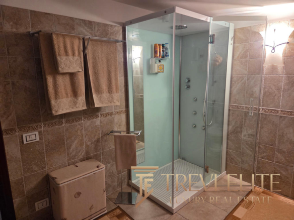 Shower enclosure in a modern bathroom with beige tiled walls, towel racks, and elegant lighting.