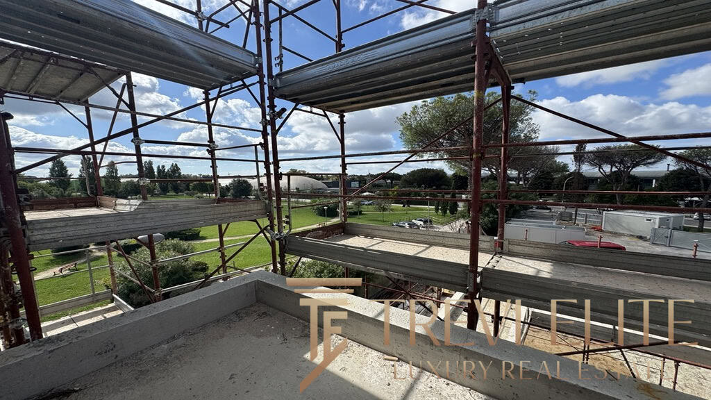 Scaffolding on a building site with a view of green parks and trees, under a partly cloudy sky, illustrating ongoing construction or renovation work in a scenic area.