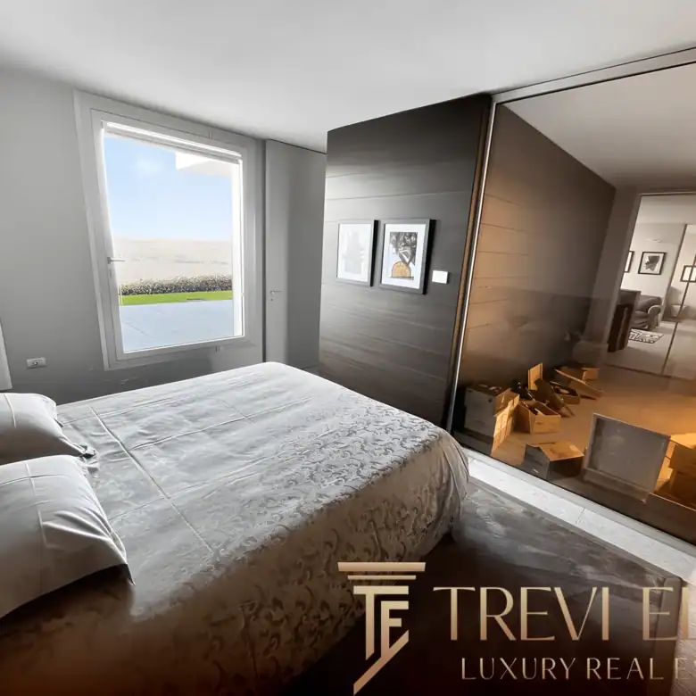 Minimalist bedroom with neutral linens and a wide window overlooking the lake.