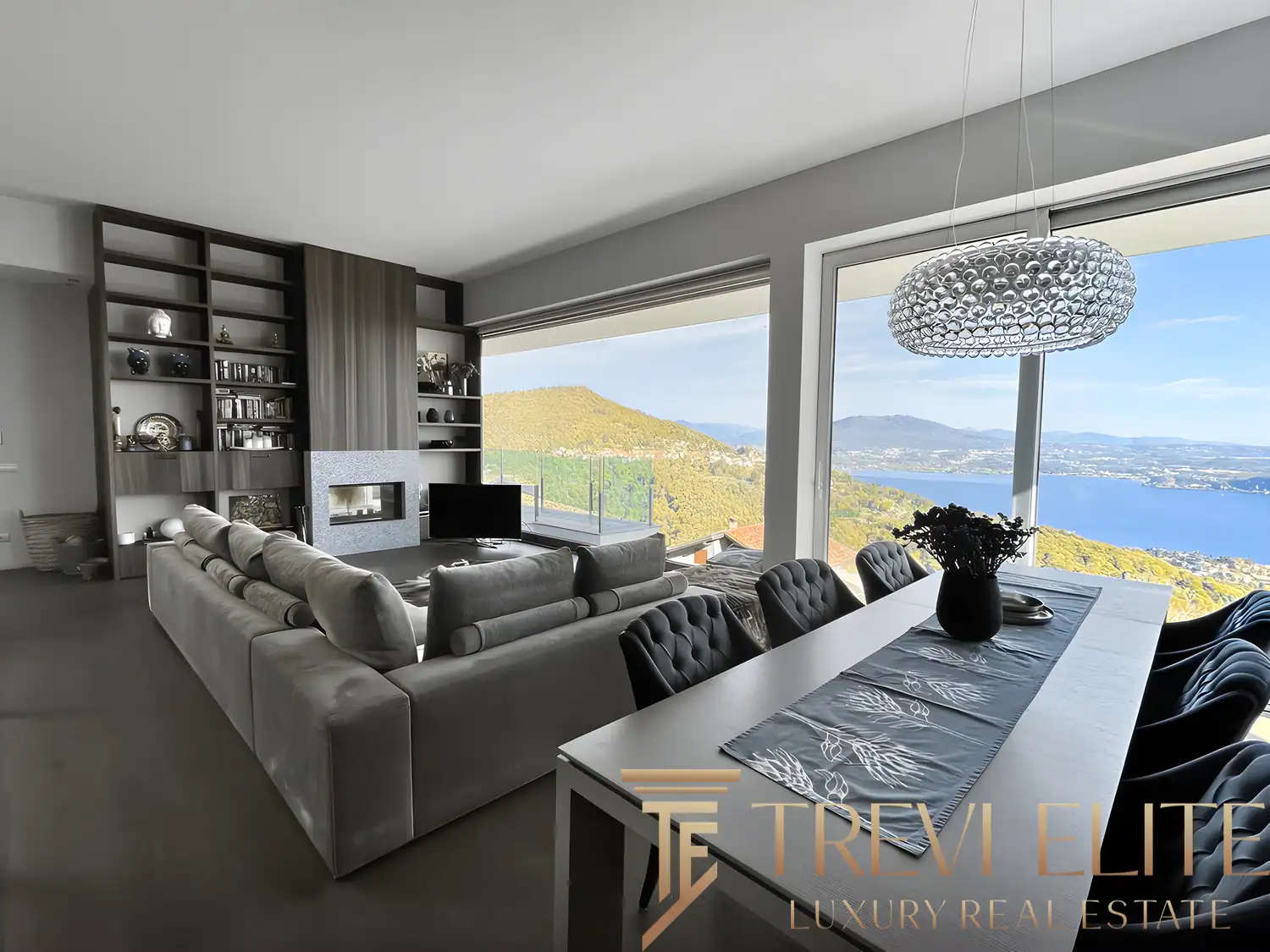 Dining table set for six with a modern chandelier and lake panorama.