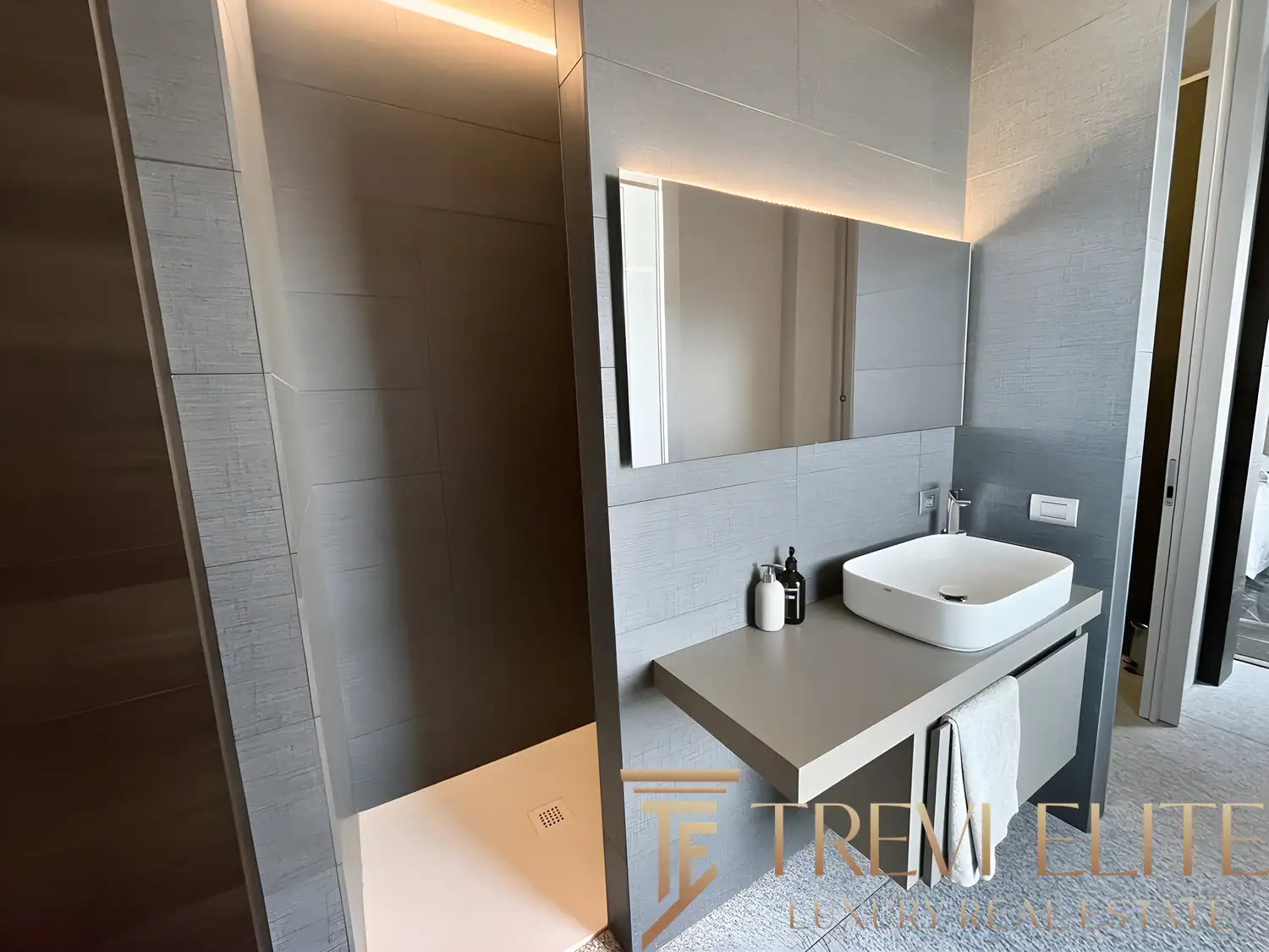 High-end bathroom with a white vessel sink, large mirror, and warm lighting.