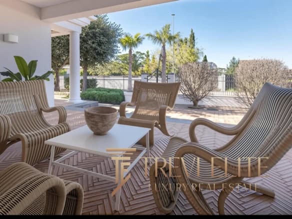 Elegant outdoor lounge area with modern wooden furniture and lush garden views in an upscale Italian real estate property. Perfect for relaxation and outdoor entertaining.