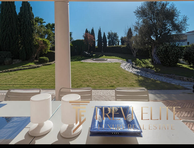 Expansive outdoor garden with lush greenery, mature trees, and stone pathways, viewed from a luxurious terrace with outdoor seating and elegant decor. Perfect for relaxing and enjoying nature.