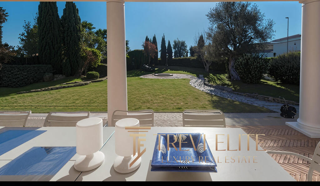 Expansive outdoor garden with lush greenery, mature trees, and stone pathways, viewed from a luxurious terrace with outdoor seating and elegant decor. Perfect for relaxing and enjoying nature.