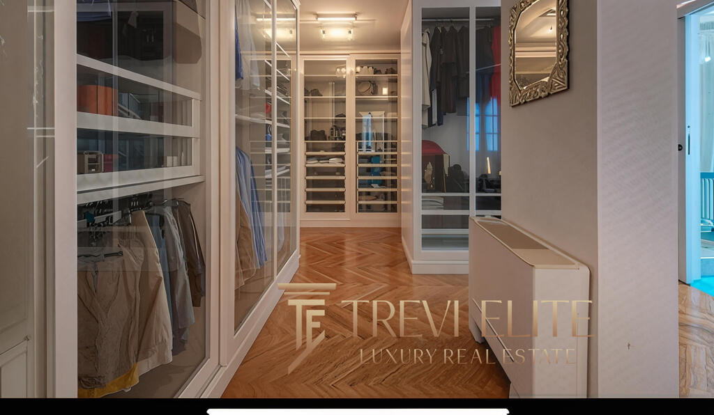 Luxurious walk-in closet with elegant glass doors showcasing neatly organised wardrobe space and wooden flooring, exemplifying high-end Italian real estate design and premium finishes.