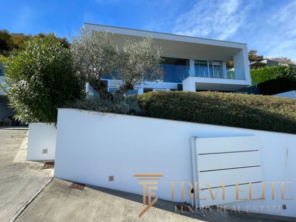 Luxurious modern island villa with sleek architecture and expansive glass windows, set on a hillside with lush greenery and a panoramic sea view, featuring a spacious terrace and contemporary design elements.
