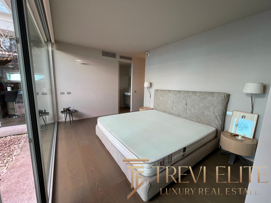 Modern bedroom with large glass doors opening to a private outdoor space, featuring minimalist furniture, neutral tones, and contemporary decor for luxurious Italian living.