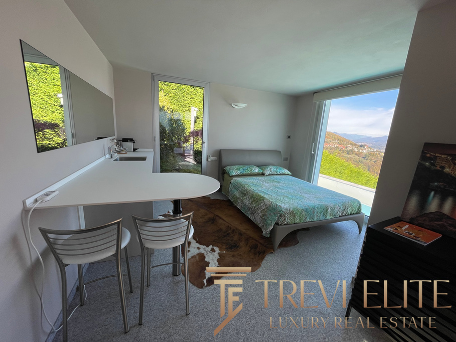 Bright modern bedroom with large windows offering scenic views of Italian landscape, equipped with a stylish bed, contemporary furnishings, and natural lighting.