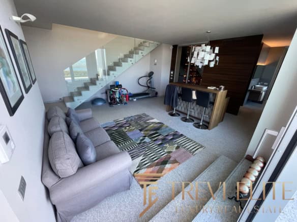 Modern living room with a grey sofa, colourful rug, and bar area in a luxurious Italian villa, featuring stylish decor, staircase, and fitness equipment for a premium lifestyle.