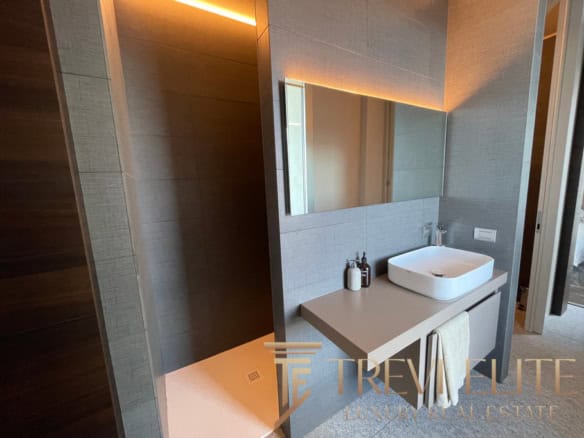 Contemporary bathroom with modern vessel sink, large mirror, soft ambient lighting, and sleek grey tiling, reflecting luxurious Italian real estate standards.