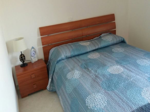 Modern bedroom with a wooden headboard and matching bedside table featuring a lamp and clock, showcasing Italian elegance and comfort.