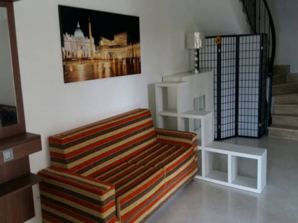 Modern living room interior with a colourful striped sofa, decorative shelving unit, artwork depicting iconic Italian landmarks, and a stylish privacy screen near a staircase.