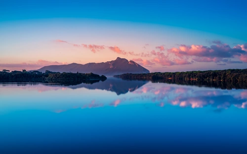 Sunset over Lake Paola in Sabaudia with Mount Circeo reflected in the calm blue water.