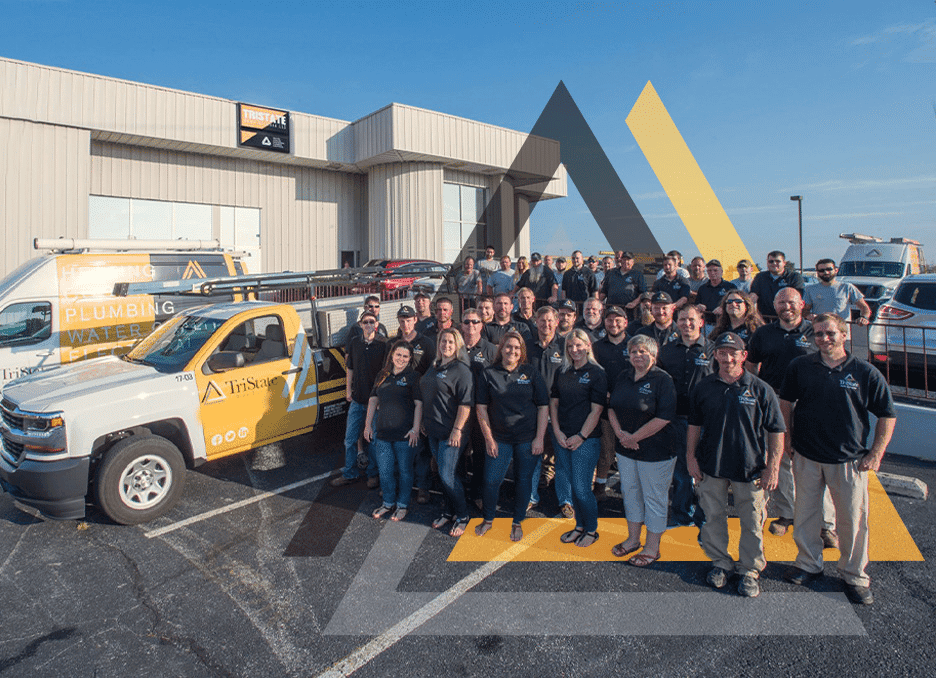 Group Of People Wearing Matching Shirts Stand In A Parking Lot Beside A Branded Company Truck With A Plumbing Logo, In Front Of A Commercial Building.