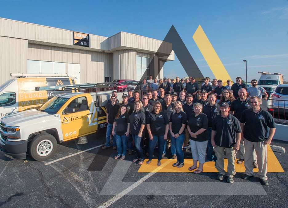 A Large Group Of People In Matching Shirts Poses In Front Of Branded Trucks And A Building With &Quot;Tristate&Quot; And &Quot;Trust Tpl&Quot; Signage Under A Clear Blue Sky.