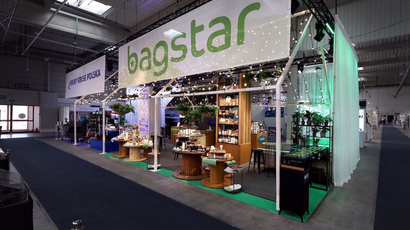 Stoisko Bagstar/Henry Kruse w konwencji stodoły - szkielet z lampkami imprezowymi, zielona paleta i zwiewne zasłony. Na Eurogastro 2026 produkty prezentowane są na drewnianych szpulach, a całość zdobią rośliny i efektowny szyld "bagstar". projekt i nadzór Tatjana Kobuszewska trksystem.com