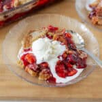 Fresh homemade cherry crumble pie topped with vanilla ice cream served on a clear glass plate, perfect for dessert lovers.