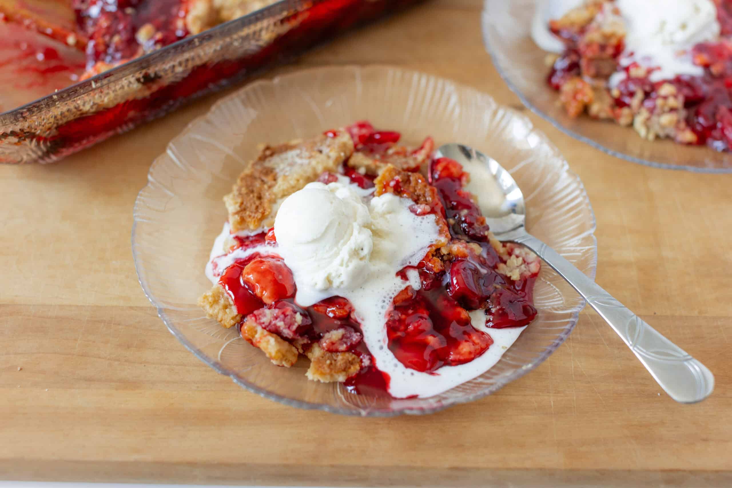 Fresh homemade cherry crumble pie topped with vanilla ice cream served on a clear glass plate, perfect for dessert lovers.