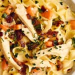 Creamy chicken and bacon fettuccine pasta with vegetables, topped with fresh herbs, served in a white bowl, delicious comfort food for easy family dinners.