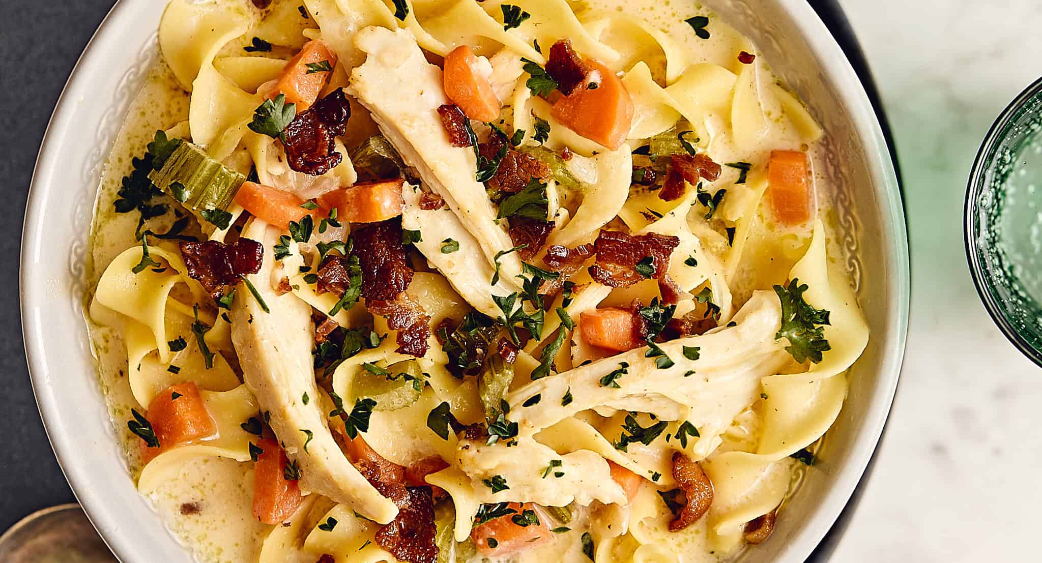 Creamy chicken and bacon fettuccine pasta with vegetables, topped with fresh herbs, served in a white bowl, delicious comfort food for easy family dinners.