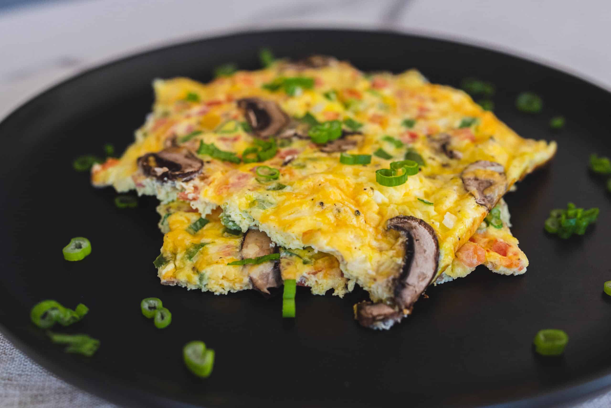 Crispy mushroom and cheese breakfast omelette with chopped green onions on black plate.