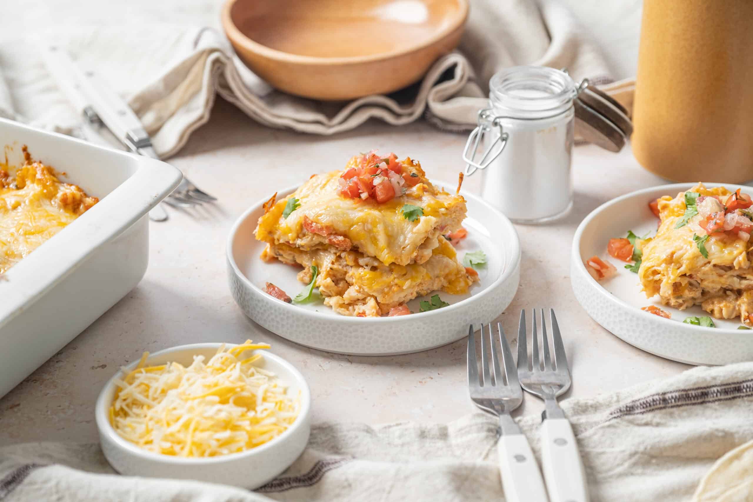Creamy chicken and cheese enchiladas topped with fresh tomatoes and cilantro on white plates at home dinner table.