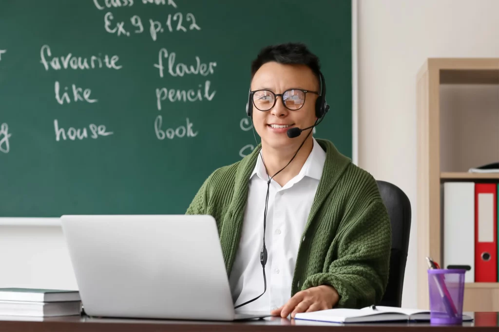 male online teacher smiling on the camera with a blackboard in the background