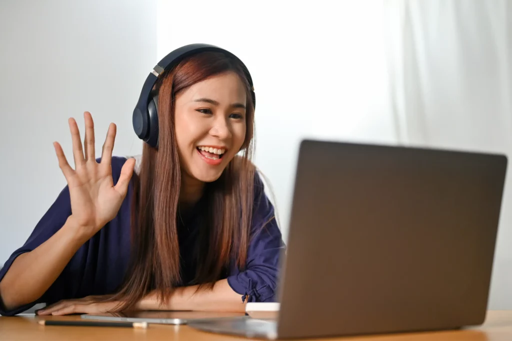 female tutor smiling and waving on a webcam