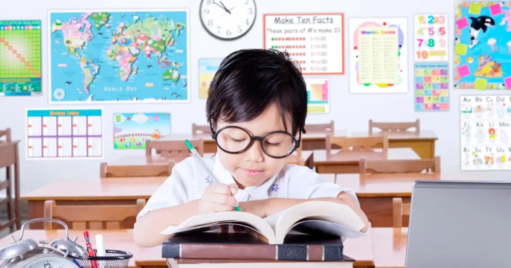 a person in glasses sitting at a desk with a laptop and books