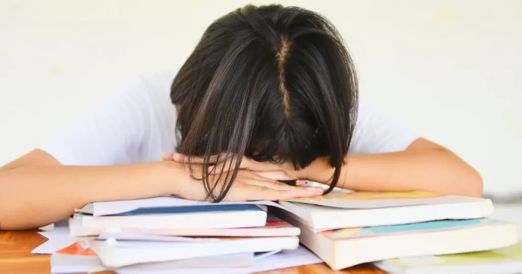 a person with their head in their hands on top of a pile of books | tuitioncentre sg