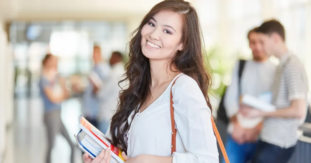A smiling person holding books in a hallway | tuitioncentre sg