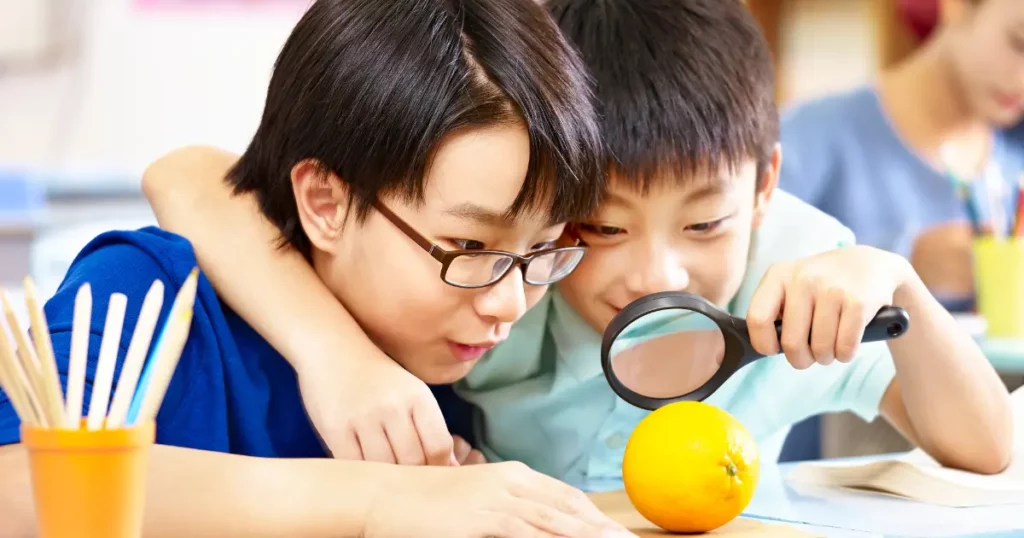two students looking at an orange through a magnifying glass | tuitioncentre sg