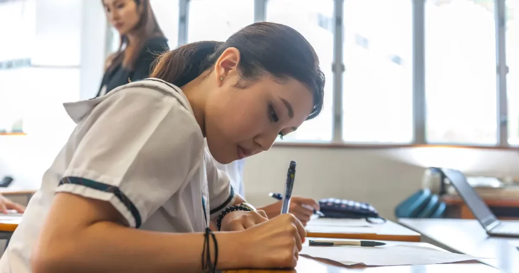 a person in a school uniform is writing on a piece of paper | tuitioncentre sg