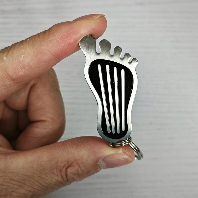 304 stainless steel Bigfoot gas pedal keychain with black stripe foot shape design.