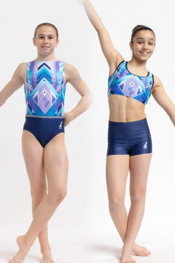 Dos gimnastas jóvenes posando de frente sobre fondo blanco; la de la izquierda lleva un justaucorps de estampado geométrico en tonos azul y morado y la de la derecha un top deportivo y shorts a juego con el mismo diseño, ambas de pie en posición de baile mostrando el logotipo de la marca.