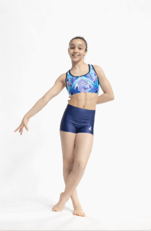 Gimnasta de pie en pose frontal, luciendo el top Geo Ice con estampado geométrico azul y malva y shorts azul marino sobre fondo blanco.