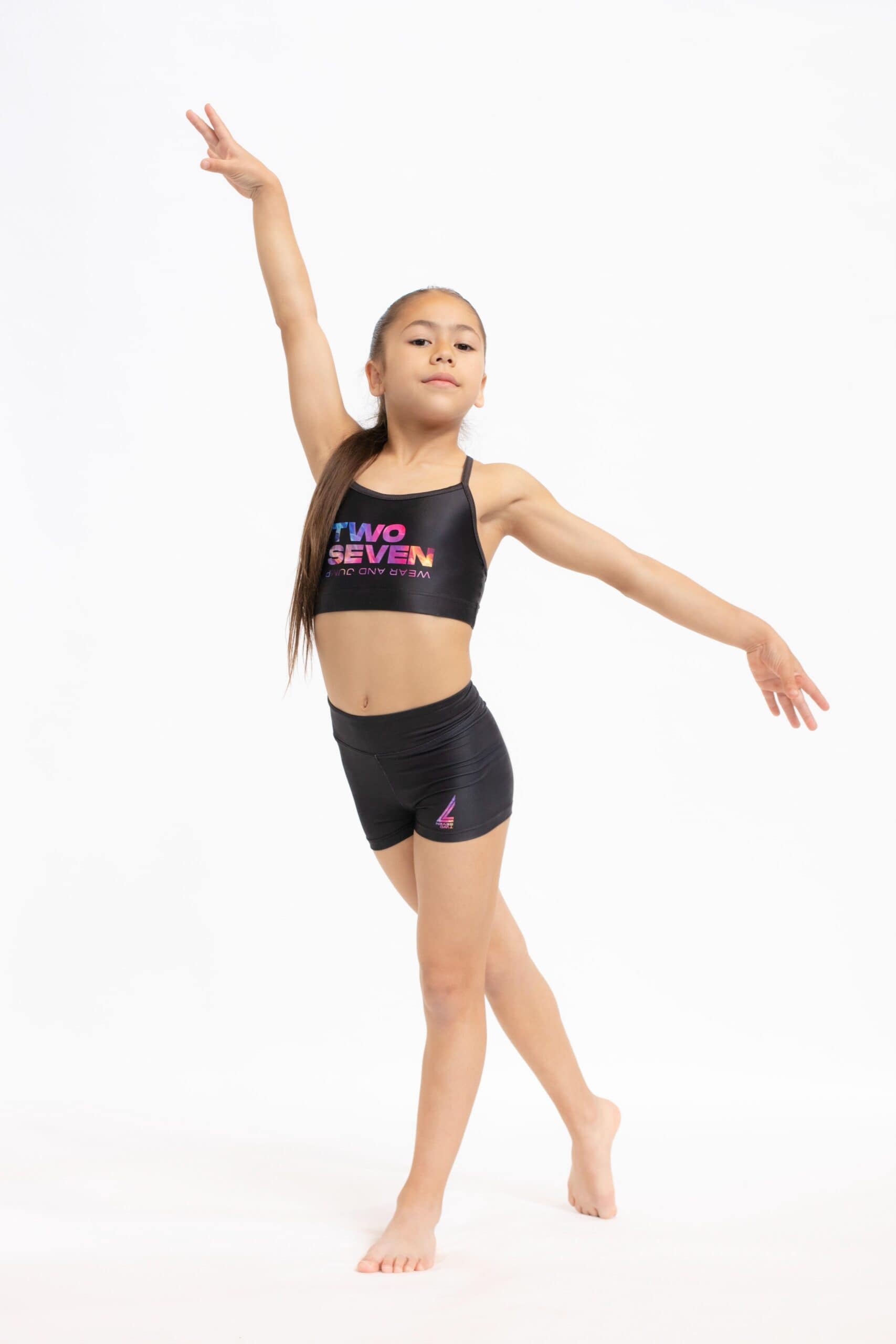 Gimnasta en pose asimétrica con un brazo levantado, vistiendo el top TWO7-1 y shorts negros