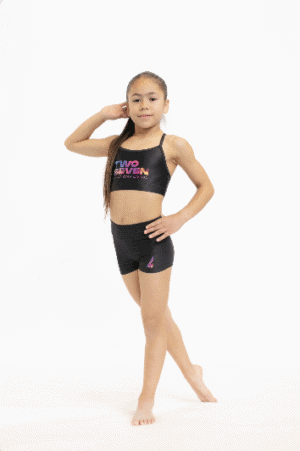 Gimnasta de pie en pose completa, luciendo el top TWO7-1 y shorts negros a juego