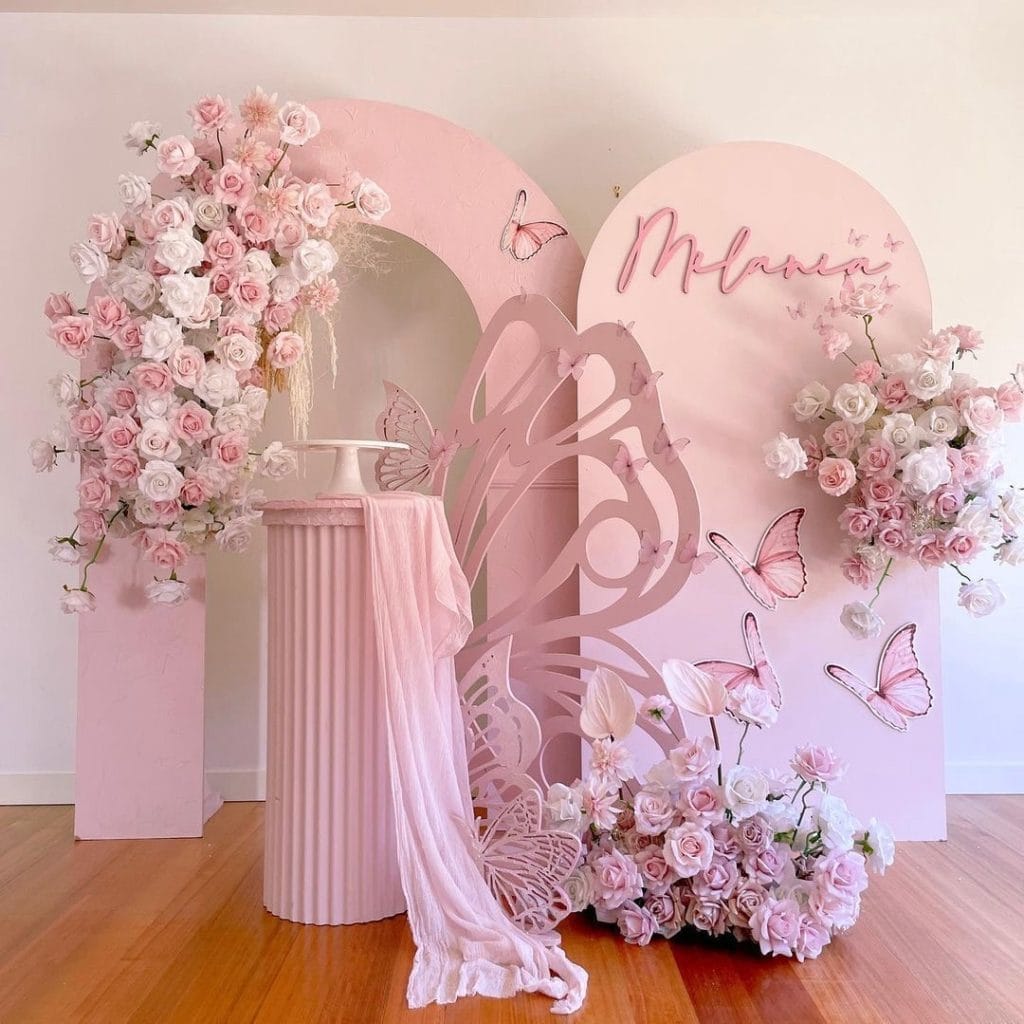 Pink floral event decoration with roses, butterflies, and elegant backdrop for special celebrations.