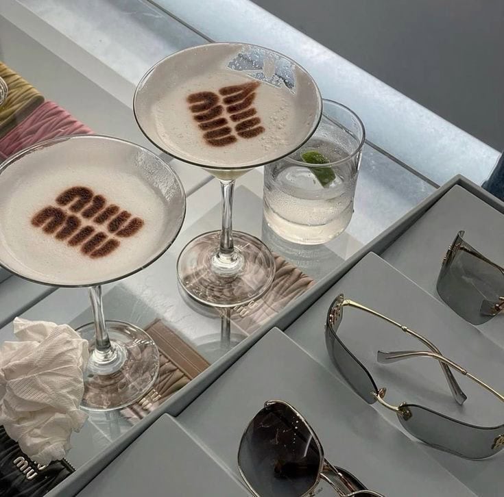 Cocktail drinks with latte art on a white table, stylish sunglasses, and a glass of sparkling water at UpEventi event venue.