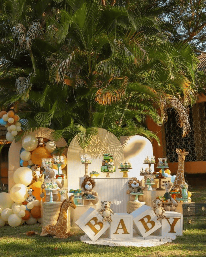 Giraffe plush toys and jungle-themed baby shower decoration under green tropical trees.