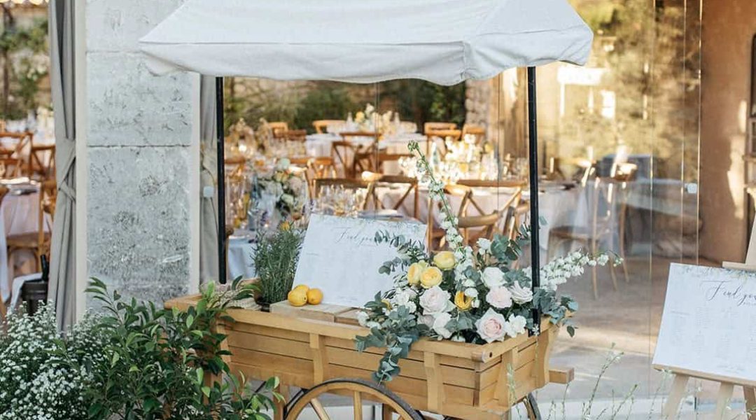 Charming outdoor event space with floral decor, string lights, and vintage cart in a natural setting.