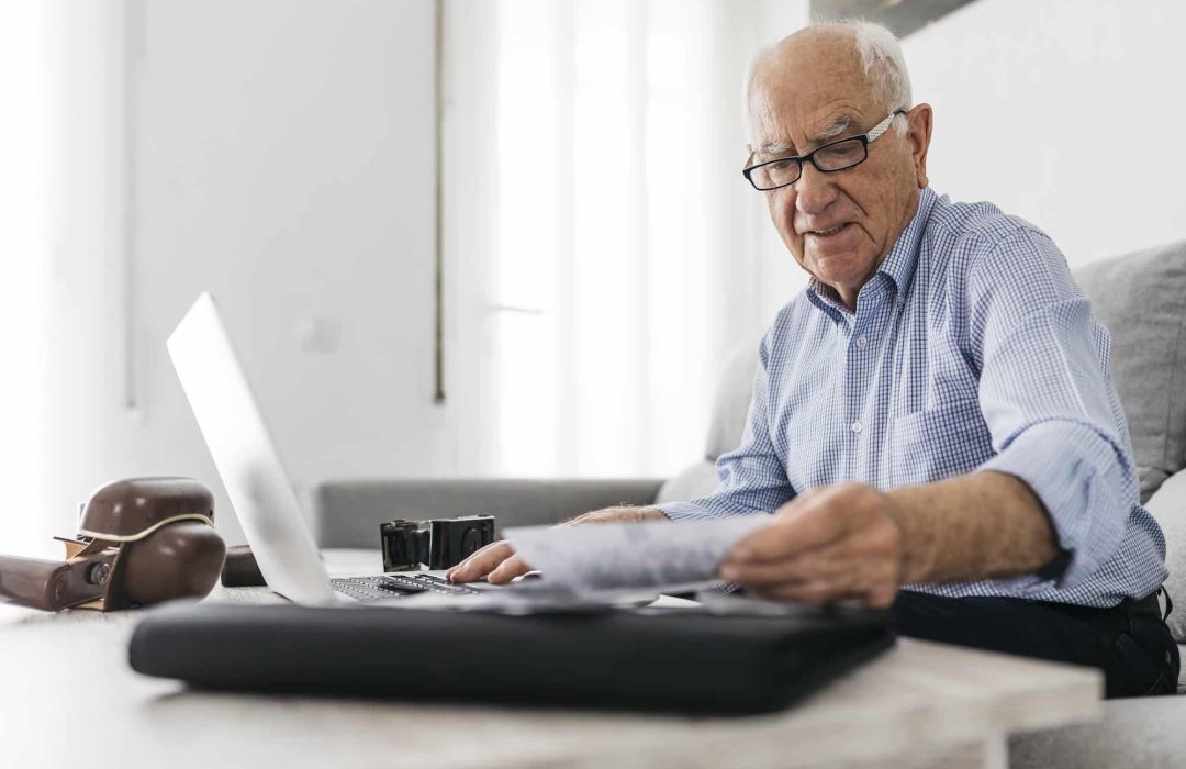 Senior man working with a computer and his old photo cameras and old photos