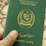 Pakistani passport with national emblem and green cover held in hand.