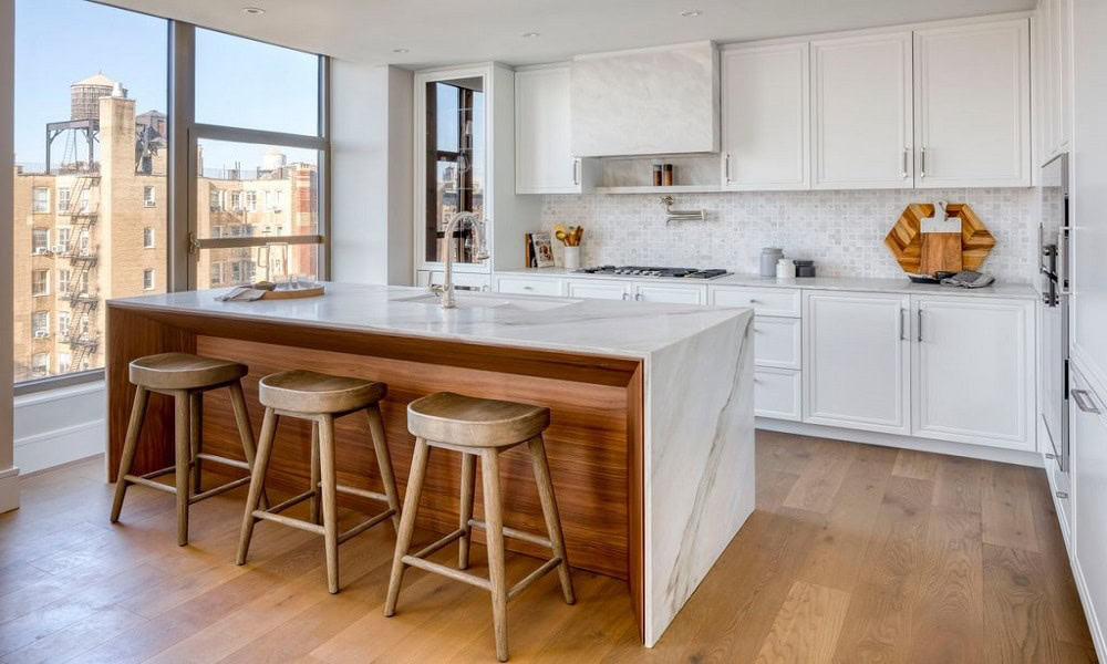 Bright modern kitchen with white cabinets, island, and wooden bar stools in urban residential settin.