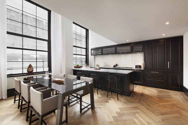 Contemporary urban kitchen with dining space, large windows, and sleek black cabinetry.