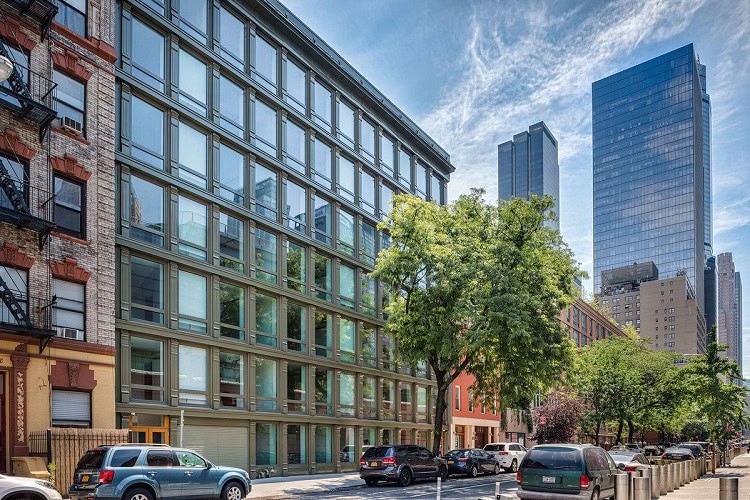 Contemporary urban apartment complex with glass facade and surrounding trees in a city setting.