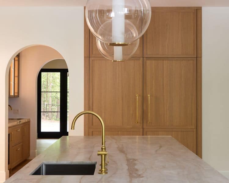 Transitional kitchen featuring sleek wooden cabinets, a marble countertop, and elegant gold fixtures.