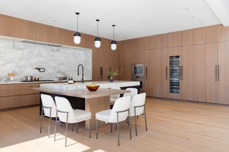 Contemporary kitchen featuring wooden cabinetry, a white island, and sleek black pendant lights for.